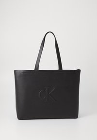 Černá kožená kabelka přes rameno se dvěma uchy, s vyraženým logem "cK" na přední straně. Hladká textura a minimalistický design.