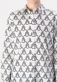 Hvit skjorte med knapper som har et svart tau-mønster. Stoffet er lett med en glatt tekstur og klassisk kragedesign.