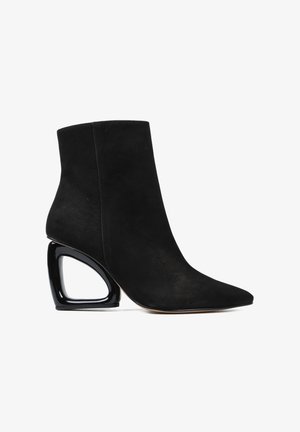 Czarne zamszowe botki za kostkę z ostrym noskiem i pustym geometrycznym obcasem w błyszczącej czarnej wykończeniu.