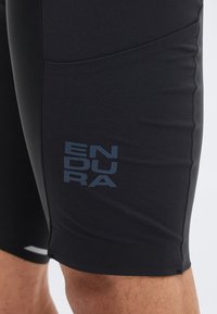 Κοντινό πλάνο ενός ατόμου που φοράει μαύρο ποδηλατικό σορτς με το λογότυπο «ENDURA» τυπωμένο στον αριστερό μηρό.