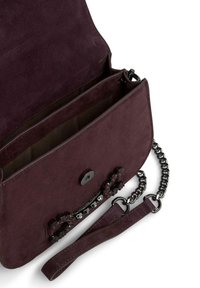 Paarse suède handtas met een zwarte kettingstrap, metalen hardware en juweelaccenten aan de voorkant. Het interieur heeft twee compartimenten.