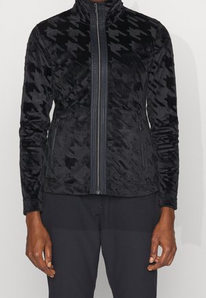 Veste noire zippée avec motif pied-de-poule texturé, col montant et poches latérales zippées portée par une personne montrée du cou aux hanches.