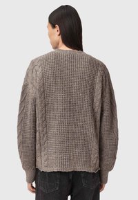 Strikkegenser i beige med teksturerte kabelstrikk-detaljer på ermene, avslappet passform, ribbestrikkede mansjetter og rå kantdetaljer.