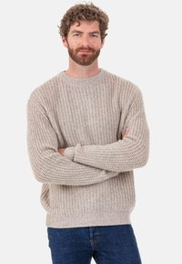 Beiger, grob gestrickter Pullover mit rundem Ausschnitt und gerippten Bündchen; kombiniert mit dunkelblauen Jeans, die eine lockere Passform und ein strukturiertes Muster aufweisen.
