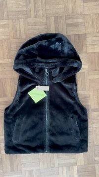Schwarze Kunstfellweste mit Kapuze, ausgestattet mit einem Vorderreißverschluss und zwei Vordertaschen. An einem Etikett ist der Markenname "even&odd" befestigt.