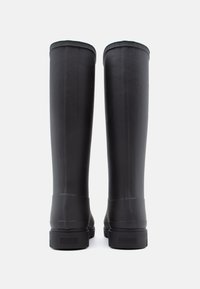 Black rubber knee-high boots with a smooth finish, vertical ridges, a rounded top, and a low textured sole. Branding visible on the heel.