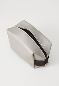 Grijze siliconen toilettas met een gestructureerde vorm, ritsluiting en een accentriem van stof. Glad oppervlak en minimalistisch ontwerp.