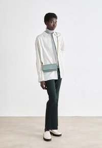 Striped white and beige oversized shirt, grey turtleneck, green pants, cream loafers, and small teal crossbody purse with gold hardware.