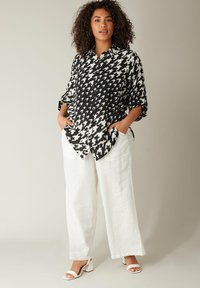 Camisa de patrón de espiga en blanco y negro, de manga larga, con bolsillos delanteros, combinada con pantalones de lino blancos sueltos y sandalias blancas de tacón bloque.