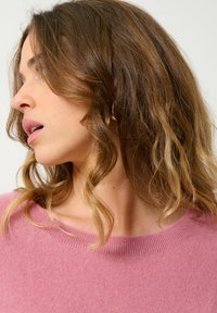 Suéter de punto rosa con un escote amplio, textura suave y un corte relajado, con un sutil borde acanalado alrededor del cuello.
