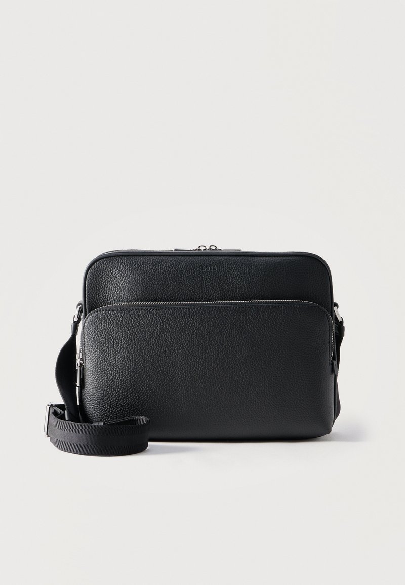 Μαύρο τσάντα χιαστί από δέρμα με υφή, με δύο διαμερίσματα με φερμουάρ και ρυθμιζόμενο ιμάντα ώμου, σε απλό ανοιχτόχρωμο φόντο.