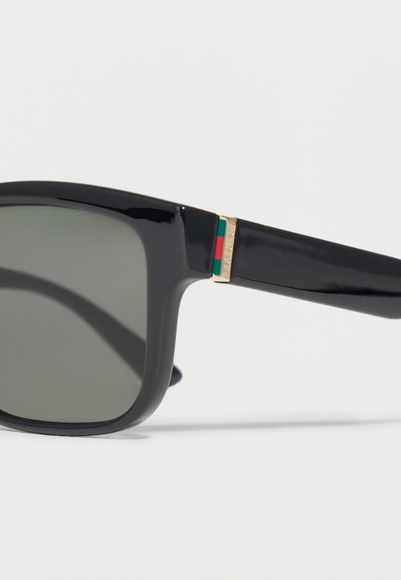 Black rectangular sunglasses with dark lenses and a gold hinge accented by green and red stripes on the temple arm.