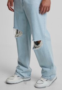 Light blue distressed jeans with frayed patches and a relaxed fit, paired with white sneakers featuring gray accents and textured soles.