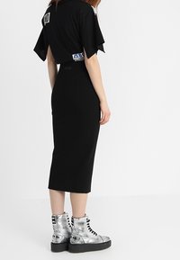 Svart midi-klänning med korta volangärmar, silverfärgade metallic kängor med svarta snören och en texturerad yta.