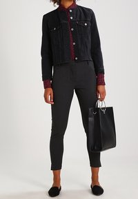 Svart denimjacka, bordeauxmönstrad skjorta, mörka slim-fit byxor, svarta platta skor, håller en svart läderhandväska med silverdetaljer.