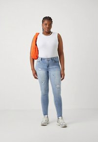 Ανοιχτό μπλε στενά τζιν με σκισίματα, συνδυασμένα με λευκή αμάνικη μπλούζα. Μια πορτοκαλί τσάντα ώμου με γέμισμα και γκρι αθλητικά παπούτσια ολοκληρώνουν την εμφάνιση.