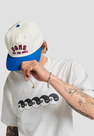 Cappello bianco e blu con il testo "VANS OFF THE WALL". T-shirt grigia con una grafica di sette volti in bianco e nero con occhi, maniche corte.
