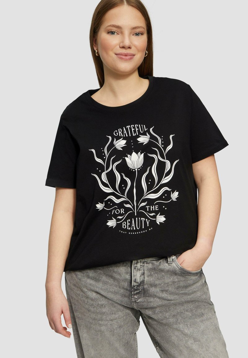 T-shirt en coton noir arborant un design graphique textuel floral blanc portant l'inscription « RECONNAISSANT POUR LA BEAUTÉ » entouré de lignes et de points.