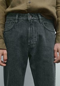 Jeans in denim grigio scuro con un classico design a cinque tasche, chiusura con bottone e leggere sfumature. La texture è liscia con dettagli di cucitura visibili.