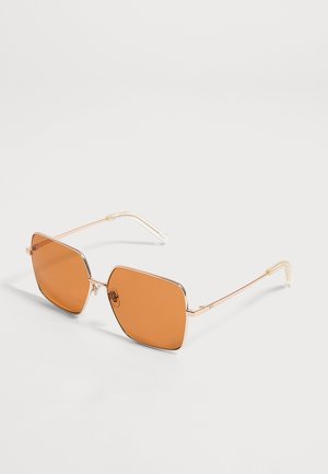 Quadratische Sonnenbrille mit dünnem goldfarbenem Metallgestell und orangefarben getönten Gläsern auf weißem Hintergrund.
