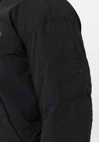 Manche de veste en nylon noir avec poche cousue comportant deux compartiments horizontaux sur le bras supérieur.