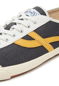 Canvas-Sneaker mit dunkelgrauem Material, kontrastierendem gelbem Zickzackstreifen, weißer Gummisohle und weißen Schnürsenkeln. Markenlogo auf der Zunge.