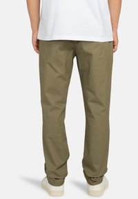 Olivegrüne Baumwollhose mit lockerer Passform, glatter Textur, geraden Beinen und einem schlichten Design. Getragen mit weißen Schuhen.