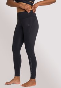 Zwarte high-waisted legging gemaakt van rekbare stof, met een logo op het linkerbeen en een soepele, strakke pasvorm.