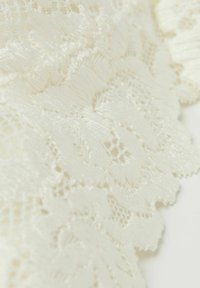 Vitt spetstyg med blommönster, intrikata detaljer och en mjuk, texturerad yta med fina trådar och öppna vävningar.