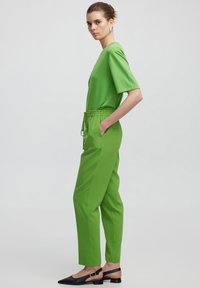 Groene shirt met korte mouwen, gecombineerd met groene, ontspannen pasvorm broek met een trekkoord in de taille en zijzakken. Zwarte platte schoenen.