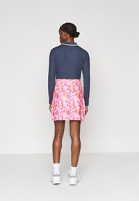 Tumesinise longi varrukatega särk, millel on sooniline tekstuur, koos roosa lillemustriga seeliku ja valgete aktsentidega. Jalas on valged tennised.