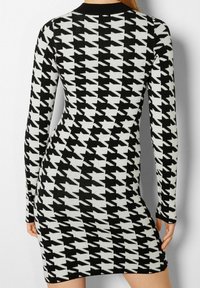 Svart och vit hounds-tooth-mönstrad stickad klänning, långa ärmar, åtsittande silhuett, rund halsringning, mjuk textur.