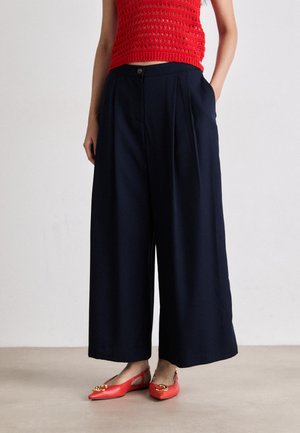 Navy wide-leg trousers with pleats and a button closure, paired with red flat shoes featuring a decorative buckle.