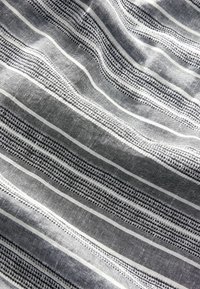 Randig tyg med djärva svarta och vita linjer i olika bredder, dekorerad med texturerade mönster och en subtil lyster.