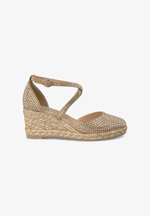 Beige espadrille-wedge met een jute zool, versierd met zilveren strass-stenen. Beschikt over een gekruiste enkelriem en een ronde neus.