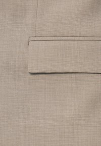 Μπεζ ύφασμα με υφασμάτινη υφή, που διαθέτει ίσια τσέπη με λεπτό άκρο στην κορυφή. Λεπτό, διακριτικό μοτίβο σε όλη την επιφάνεια.