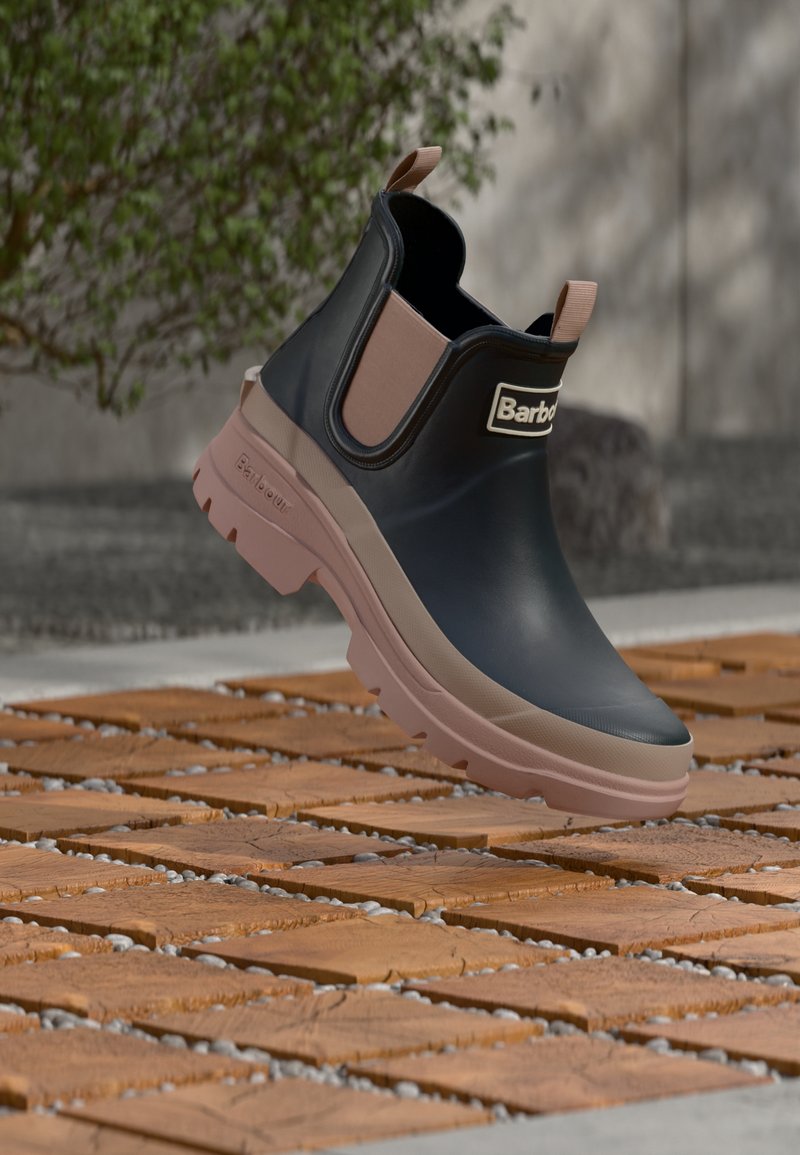 Μαύρο λαστιχένιο μποτάκι αστραγάλου με μπεζ λεπτομέρειες, διαθέτει υφασμένο πέλμα και θηλιά για εύκολο τράβηγμα. Το όνομα της μάρκας είναι τυπωμένο στο επάνω μέρος.