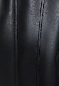 Materiale in pelle nera con una texture liscia. Presenta cuciture verticali e una tasca laterale. Design semplice e strutturato.