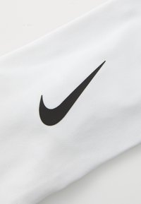 Hvit stoffarm erme med en fremtredende svart Nike swoosh-logo. Teksturen ser glatt og atletisk ut i design.