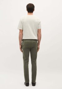 Šedé tričko s krátkým rukávem spárované s olivově zelenými slim-fit kalhotami. Kalhoty mají zadní kapsy a hnědé kovové detaily.