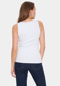 Tricou alb cu striații, cu guler rotund, design fără mâneci și o siluetă ajustată, asortat cu blugi de culoare bleu închis cu cusături în contrast.