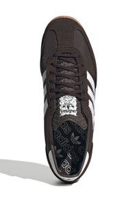 Mörkbrun sneaker med vit tre-stripesdesign, i mockamaterial, texturerad tunga och mönstrad sula med Adidas-logotyp.