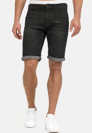 Sorte denimshorts med oprullede kanter, med forlommer og slim fit. Bæres med hvide sneakers, hvilket viser en afslappet stil.