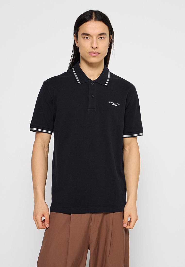 Schwarzes Poloshirt mit weiß gestreiftem Kragen und Bündchen, ausgestattet mit einer Knopfleiste mit zwei Knöpfen und gesticktem Logo auf der linken Seite.