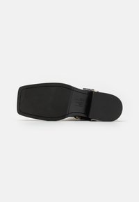 Suela de zapato negro con una textura suave, que presenta ranuras horizontales para mejorar la tracción. El diseño incluye un elegante detalle de hebilla en el lateral.