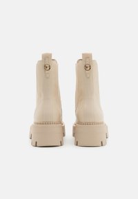 Botas de tobillo beige con un acabado suave, paneles laterales elásticos y una suela gruesa y robusta. Incluyen una pestaña trasera y detalles metálicos decorativos.