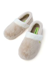 Chaussons beige moelleux avec un col blanc doux, un bout arrondi et une étiquette verte à l'intérieur. La texture en peluche offre un confort pour une utilisation intérieure.