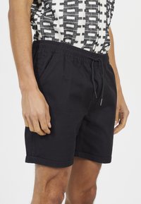 Czarne szorty wykonane z bawełny, z elastycznym pasem ze sznurkiem, bocznymi kieszeniami i zawiniętym wykończeniem.