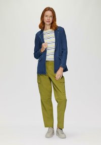 Denim blazer met notch-kleppen, gestreepte wit en gele T-shirt, olijfgroene cargobroek en lichtgrijze sneakers met dikke zolen.