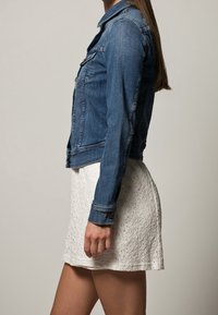 Jeansjacka i blått med två bröstfickor, knäppta manschetter och en figursydd design, kombinerad med en vit, texturerad, knälång kjol.